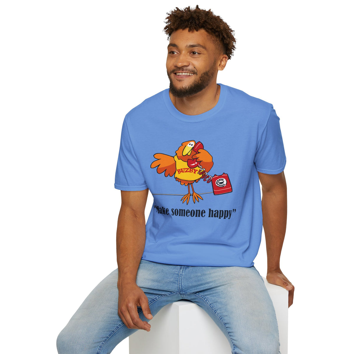 Man wearing a blue t-shirt with a cartoon Buzby character and text, sitting on a white stool against a white background.