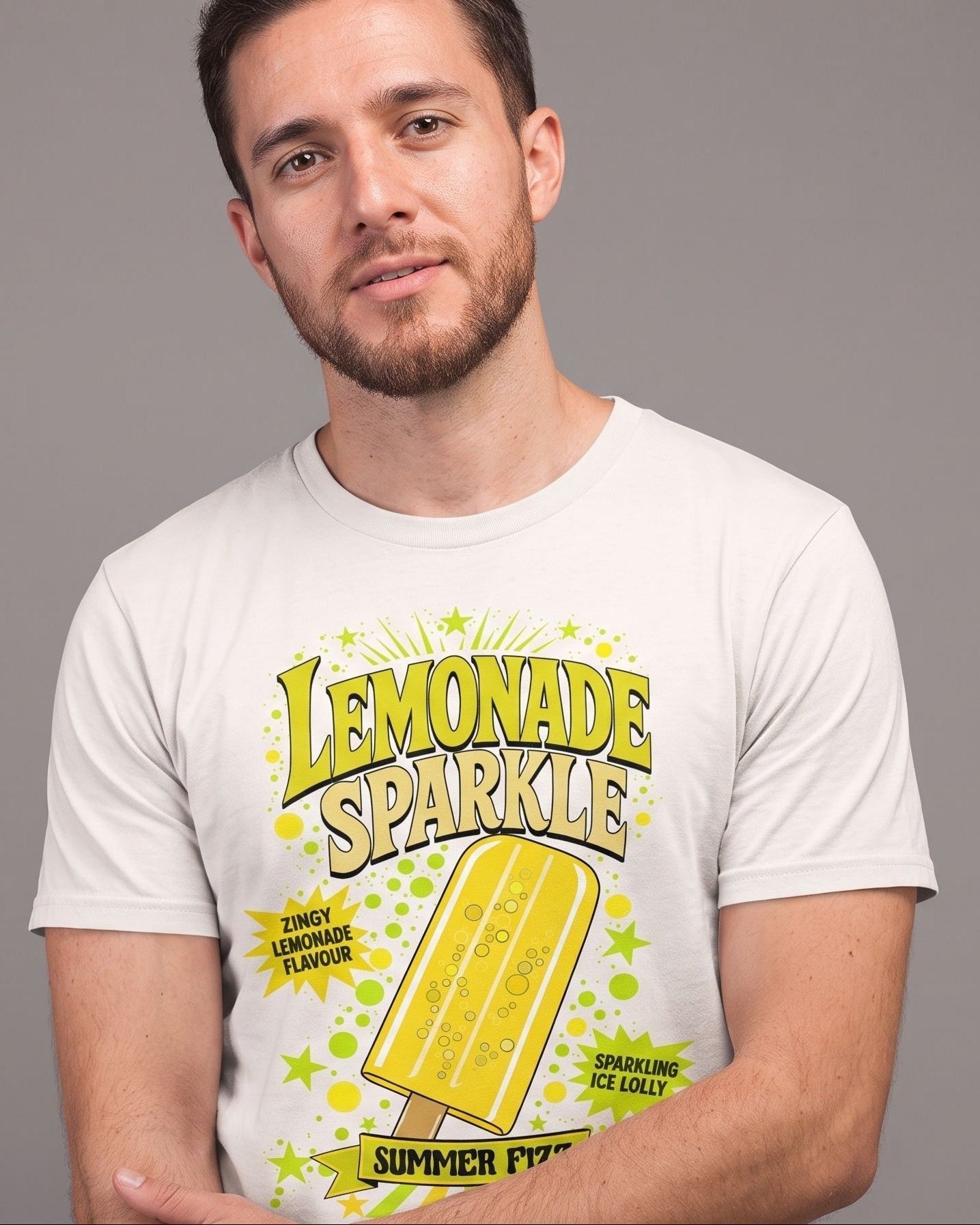 A man wearing a white graphic t-shirt with a yellow and green 'Lemonade Sparkle' summer fizzy design, posed against a solid gray studio background.