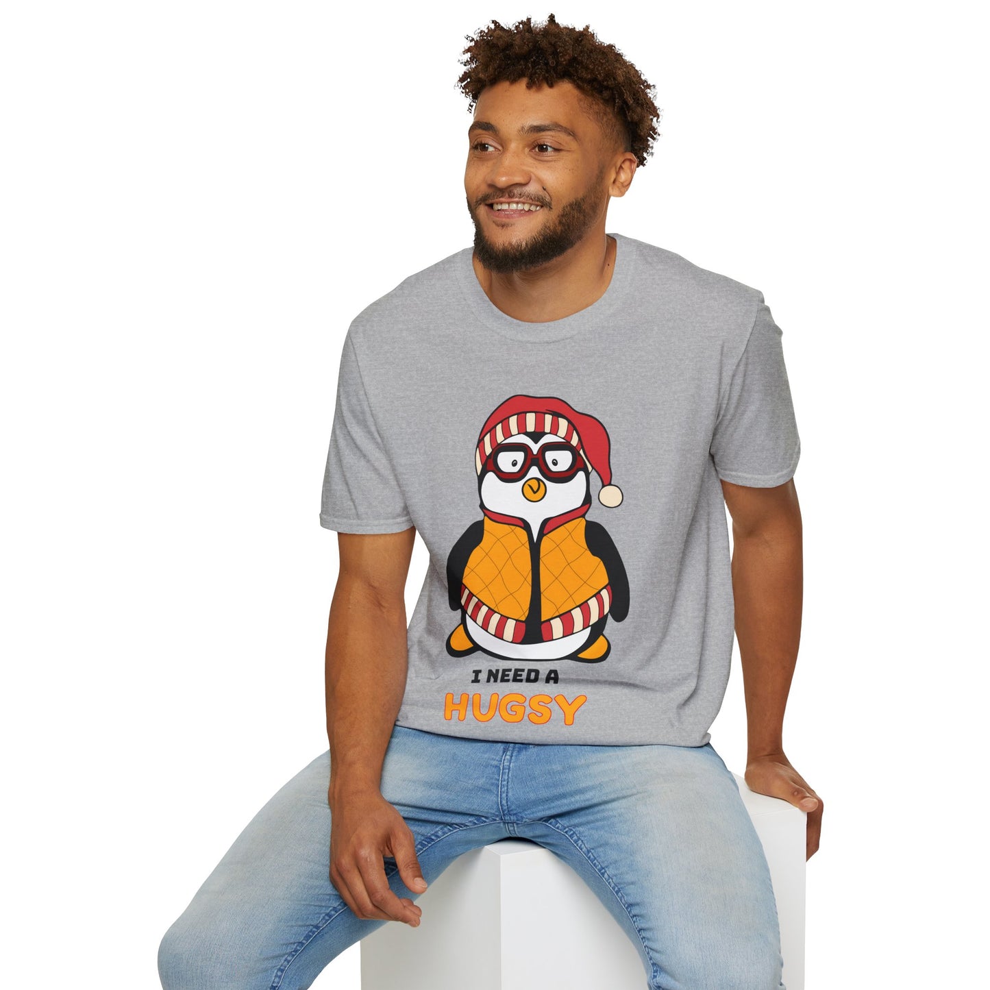 Man wearing a grey t-shirt with a penguin graphic and I Need A Hugsy text, sitting on a white stool.