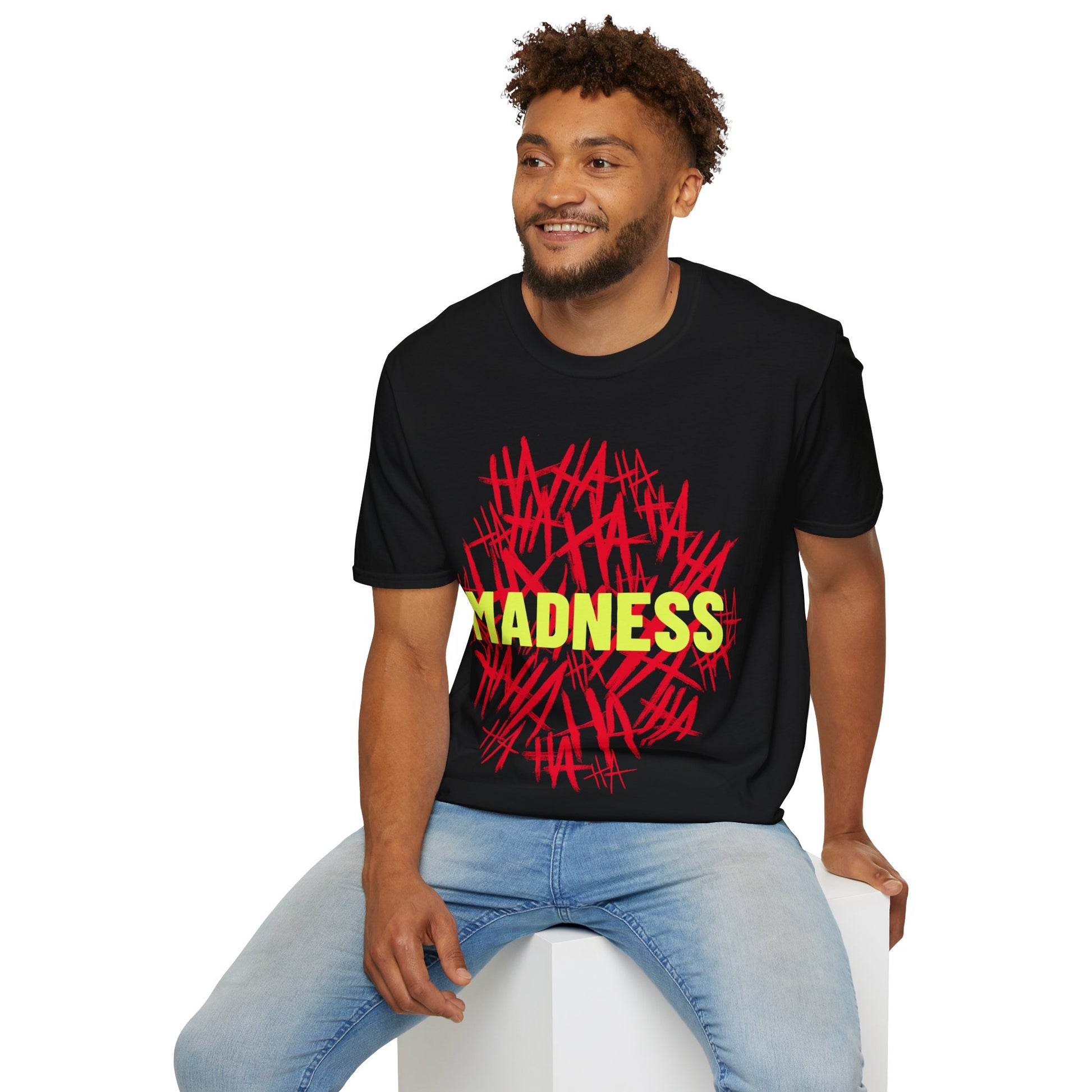 Man wearing a black t-shirt with a Joker inspired text design, red HA HA HA HA and yellow Madness graphic text design sitting on a white stool.