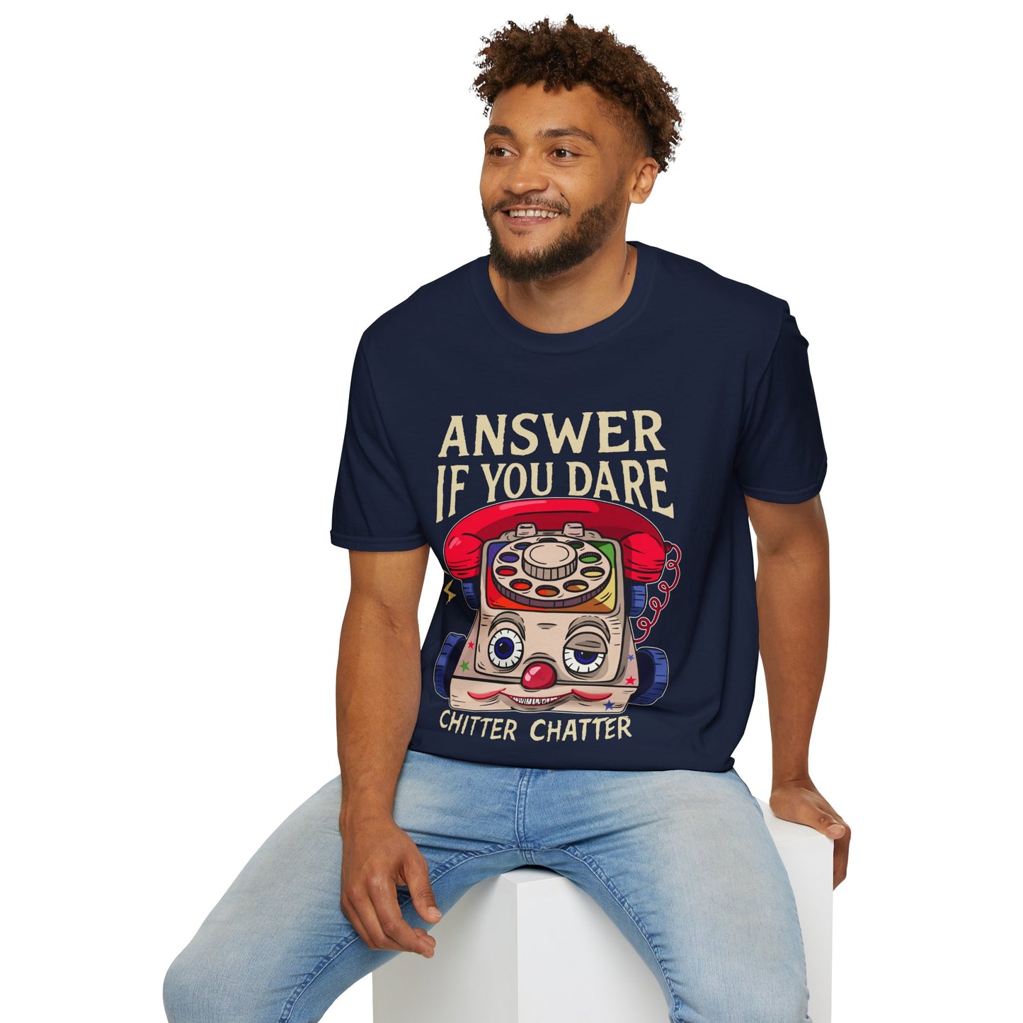 Man wearing a navy blue t-shirt with a eerie vintage toy phone graphic and Answer if you dare text,, sitting on a white stool against a white background.