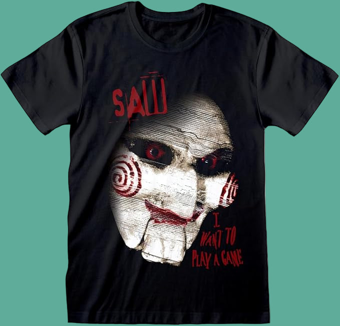 Black short sleeve T-shirt featuring a lose up eerie Saw horror movie face and I want to play a game Text, laying flat on a green backdrop