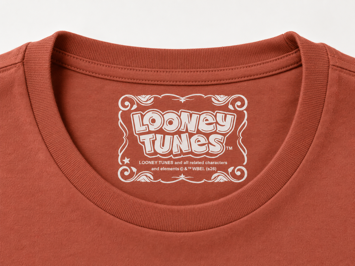 Close-up of a cinnamon coloured t-shirt collar featuring a white printed 'Looney Tunes' logo on the inside neck label.