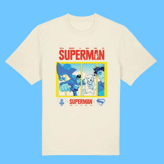 An off-white short-sleeve crewneck t-shirt featuring a colorful graphic print of Superman and other DC characters under the word 'SUPERMAN' in red, with a yellow border and small DC logos at the bottom.
