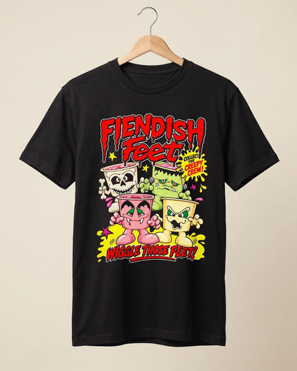 A black short-sleeve t-shirt hanging on a wooden hanger against a light beige background. The shirt features a colorful graphic print on the front with the text 'Fiendish Feet' and 'Wiggle Those Feet!' surrounding cartoonish characters in pink, green, and yellow.