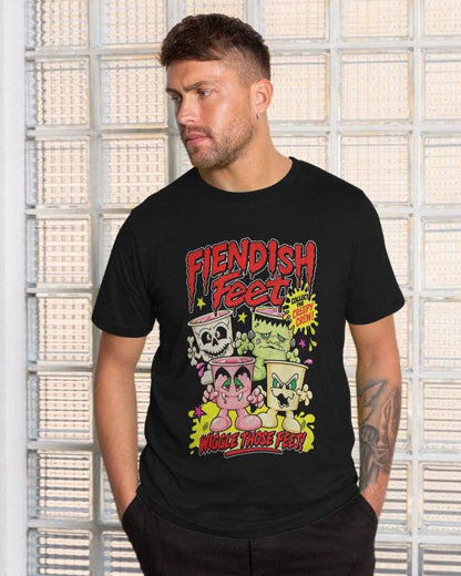 A man wearing a black graphic t-shirt with a colorful 'Fiendish Feet' cartoon design, standing in front of a glass block wall.