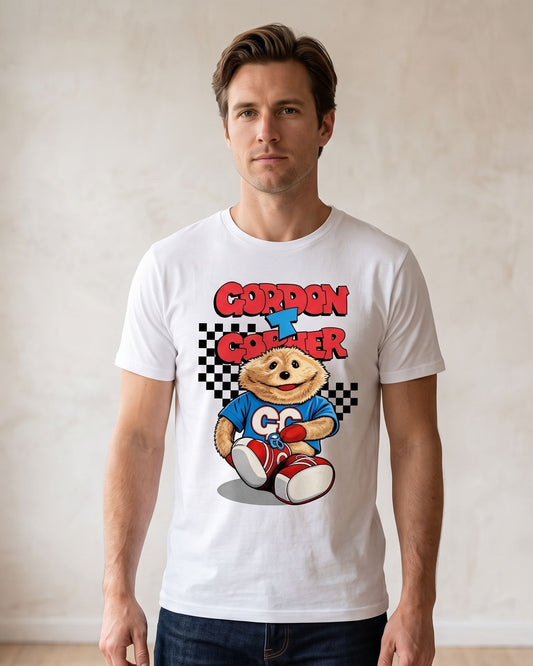 A man wearing a white short-sleeve t-shirt with a colorful retro graphic of the iconic TV broom cupboard character and the text 'Gordon T Gopher' in red and blue, standing in a brightly lit room with a textured beige wall.