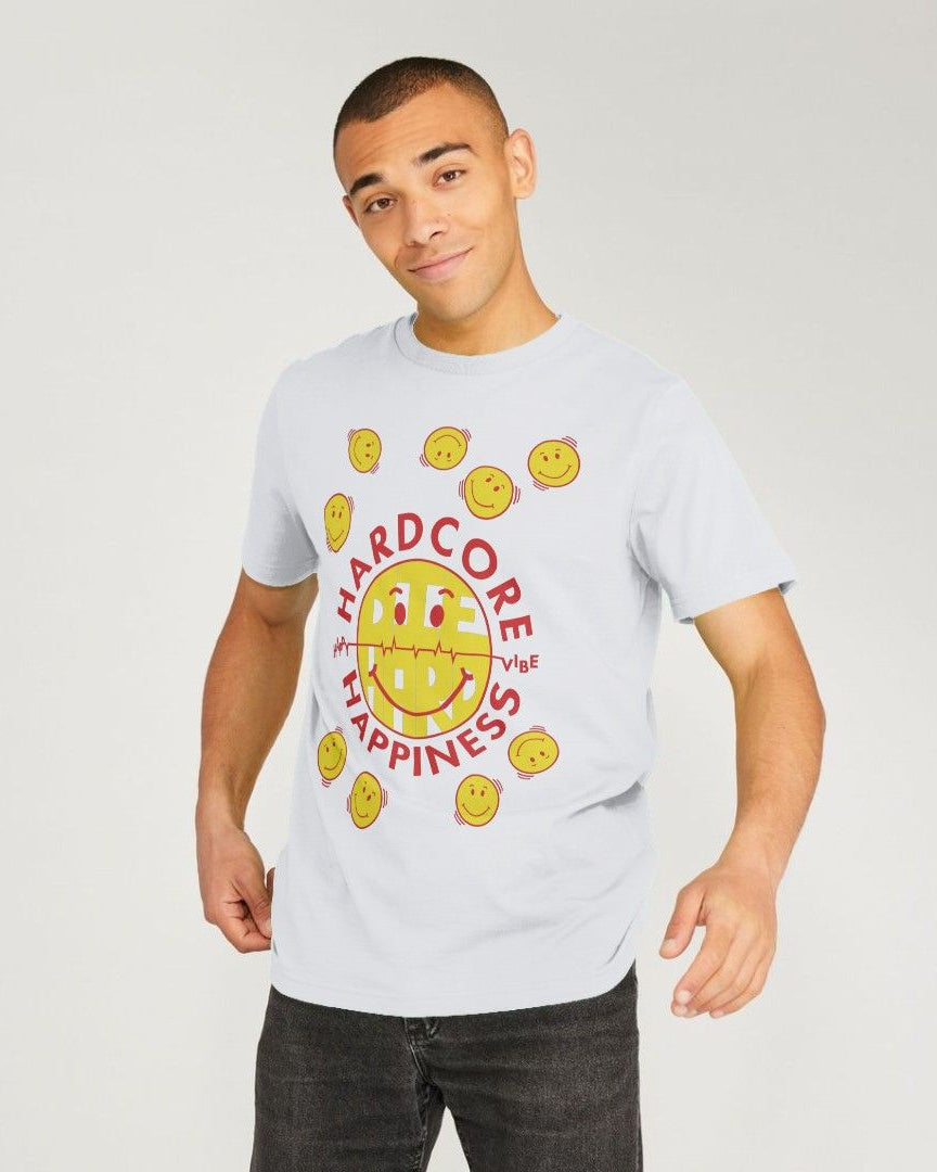 A man wearing a white graphic t-shirt with a yellow smiley face and red text reading 'HARDCORE  Happiness', paired with dark gray jeans, against a light gray studio background.