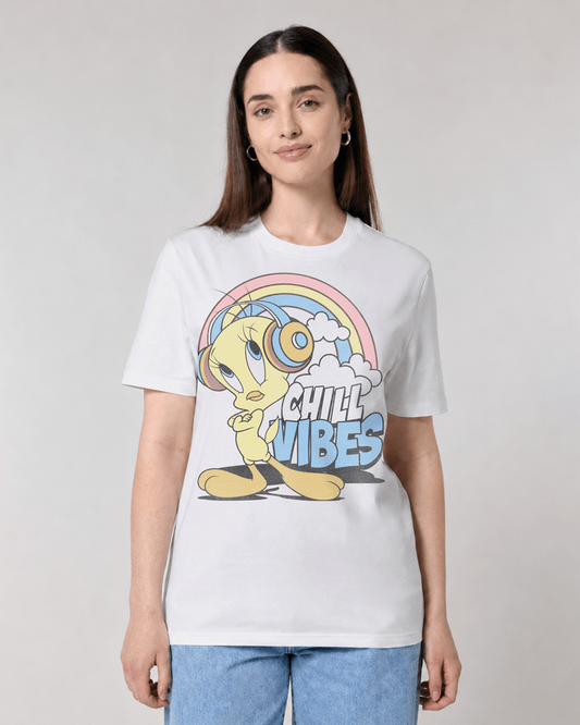 A woman modeling a white short-sleeve graphic t-shirt featuring Tweety Bird under a rainbow with the text 'CHILL VIBES' in blue and yellow, paired with light blue jeans against a light gray studio background.