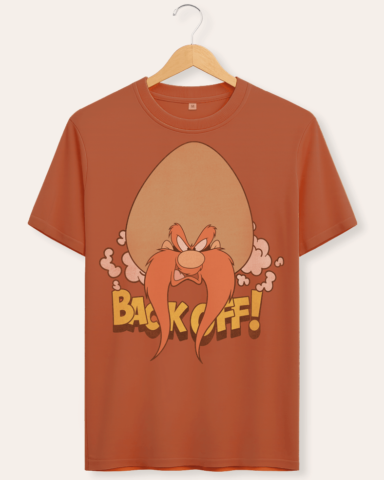 A rust-brown crewneck t-shirt hanging on a wooden hanger against a light beige background. The shirt features a graphic of the cartoon character Yosemite Sam with Back Off text in a vintage look