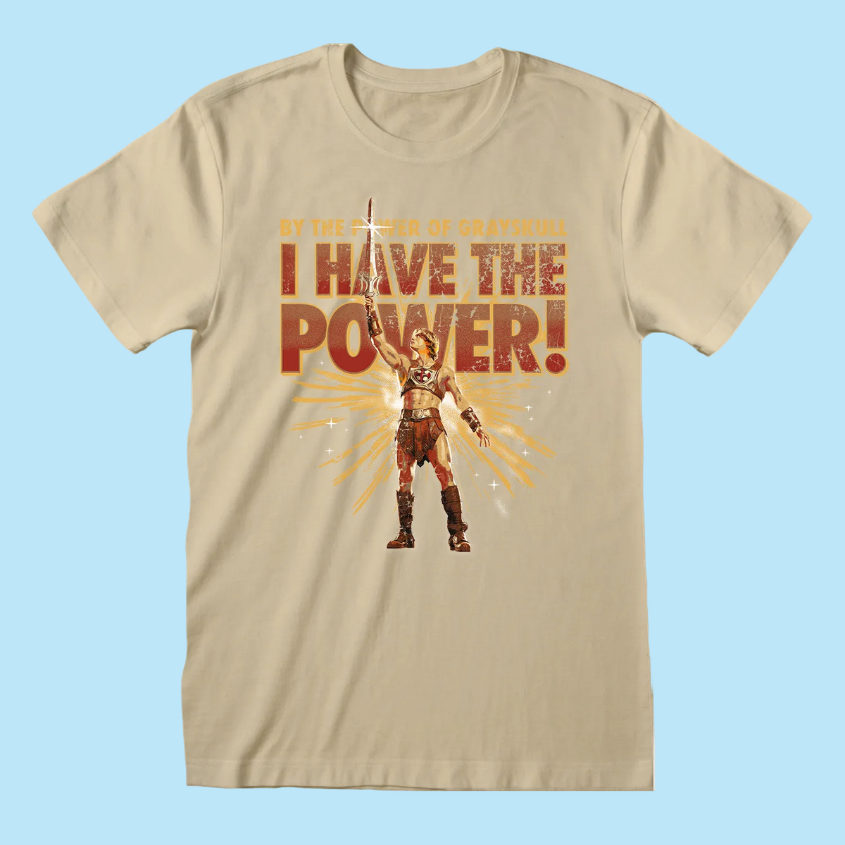 A beige crewneck t-shirt featuring a graphic print of a warrior character holding a sword, with the text 'BY THE POWER OF GRAYSKULL I HAVE THE POWER!' in distressed orange and red lettering.