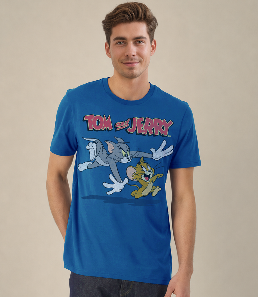 A man wearing a blue short-sleeve graphic t-shirt featuring the 'Tom and Jerry' cartoon characters, set against a plain beige studio background.