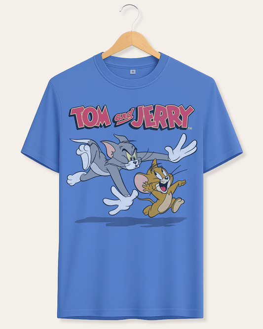 A blue short-sleeve crewneck t-shirt hanging on a wooden hanger against a light beige background. The shirt features a large graphic print of the cartoon characters Tom and Jerry running, with the 'Tom and Jerry' logo printed above them.