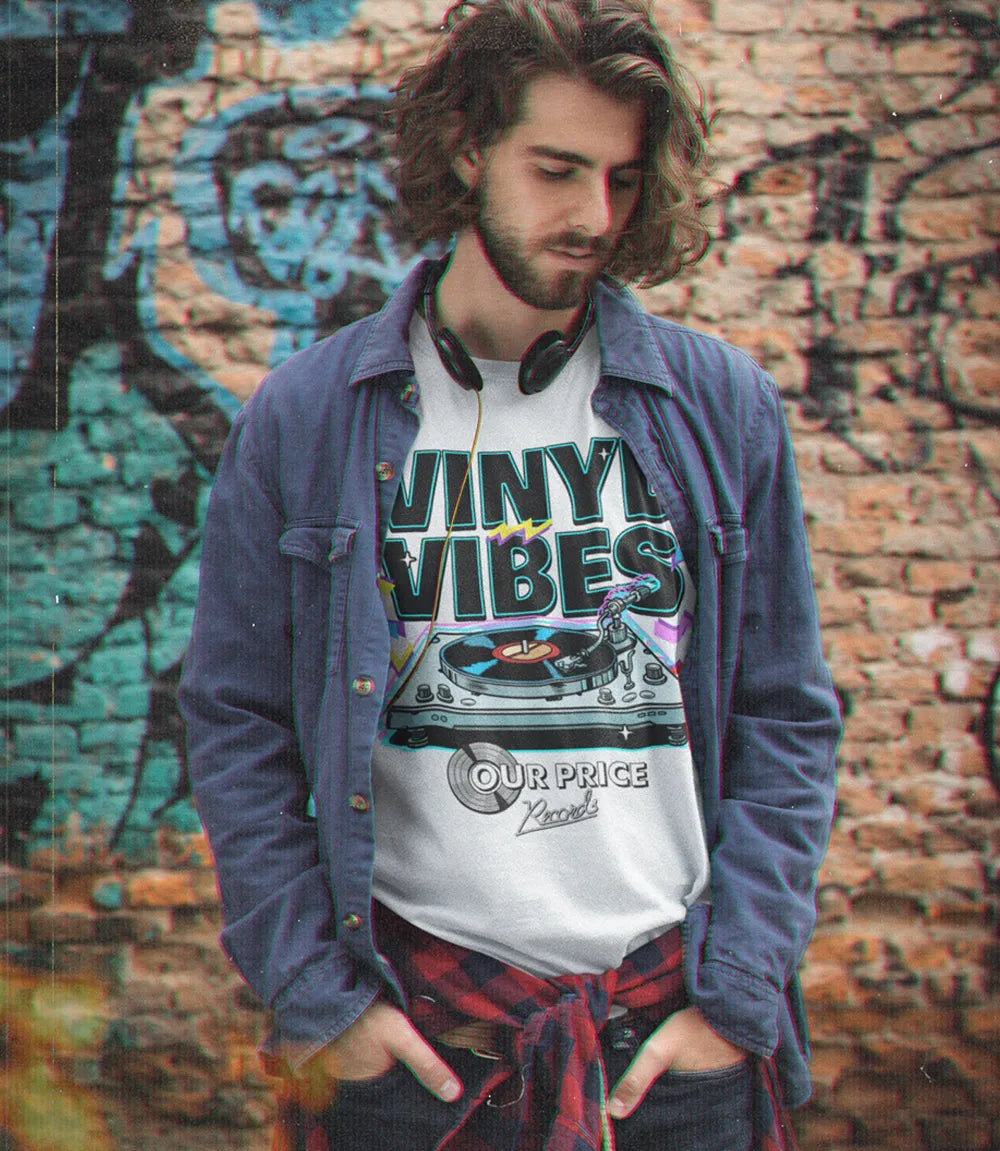man stood against brick graffiti wall wearing white short sleeve t shirt casual shirt, headphones and jeans t shirt featuring Vinyl vibes text and record player retro design with our price logo