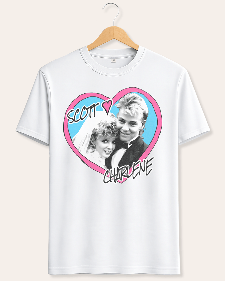 A white short-sleeve crewneck t-shirt hanging on a wooden hanger against a light beige background. The shirt features a graphic print of a heart containing a black-and-white photo of a couple, with a pink border and the words 'SCOTT' and 'CHARLENE' written in black script.
