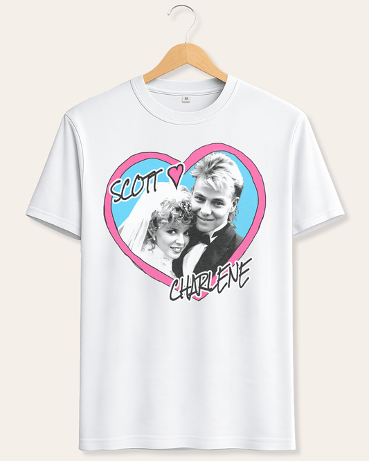 A white short-sleeve crewneck t-shirt hanging on a wooden hanger against a light beige background. The shirt features a graphic print of a heart containing a black-and-white photo of a couple, with a pink border and the words 'SCOTT' and 'CHARLENE' written in black script.