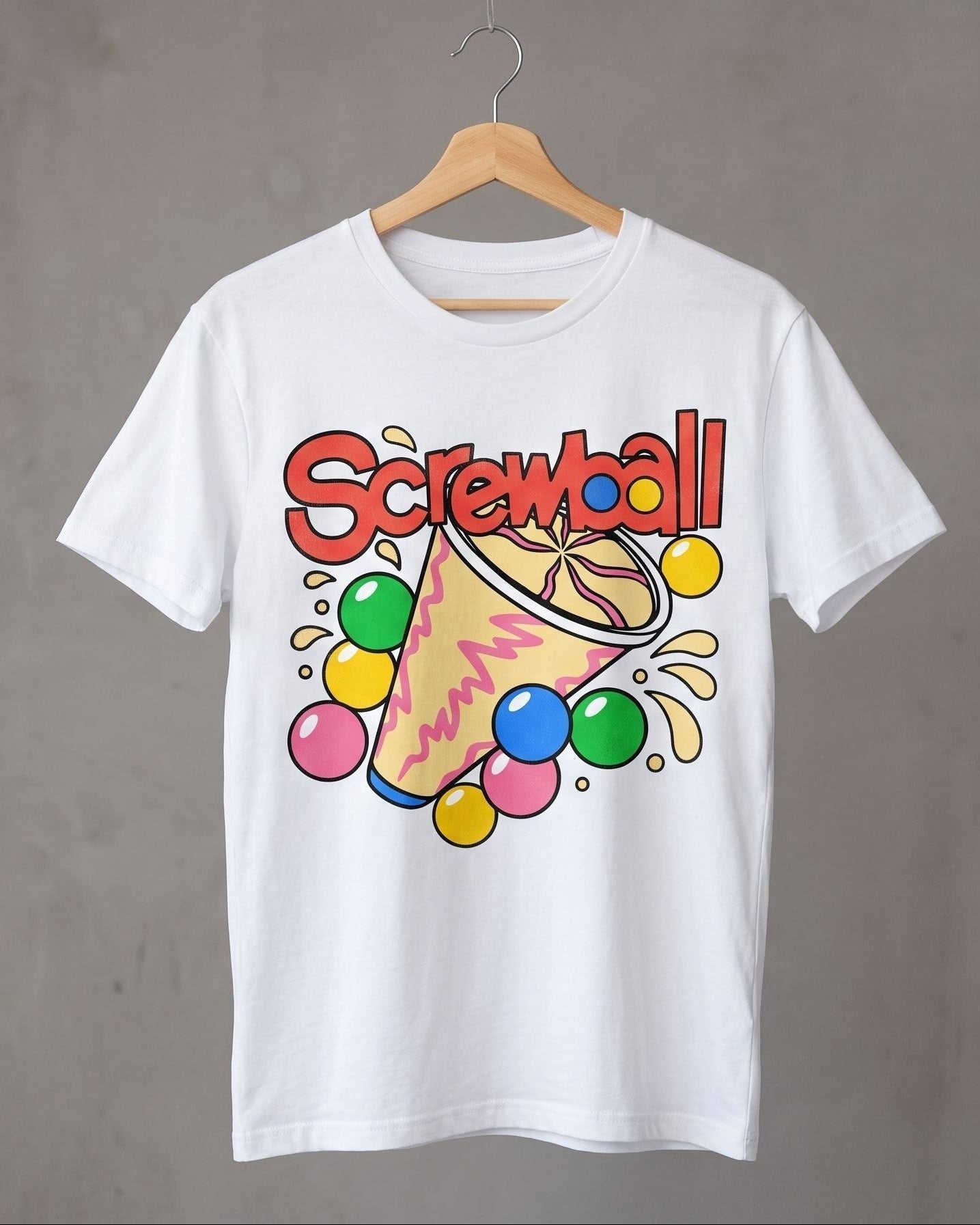 A white short-sleeve t-shirt hanging on a wooden hanger against a textured gray wall. The shirt features a colorful graphic print of a screwball ice cream with the word 'Screwball' in red letters and multicolored gumballs.