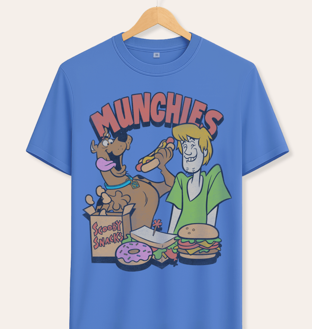 Official Scooby Doo Blue t-shirt with cartoon characters Shaggy and Scooby eating Scooby snacks and 'MUNCHIES' text above,  on a hanger against cream background