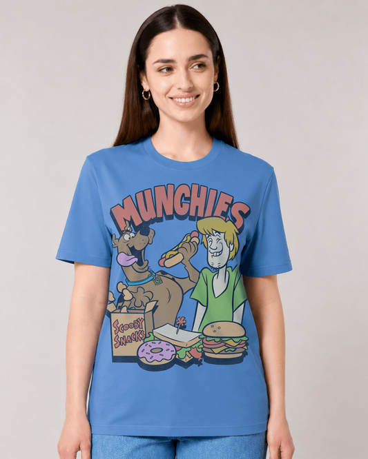 A woman modeling a blue graphic t-shirt featuring cartoon characters from Scooby-Doo and the text 'MUNCHIES' above a food spread. The background is a solid light gray studio backdrop.