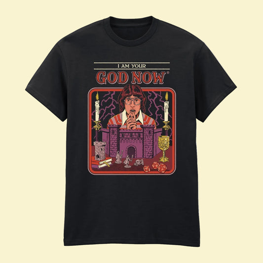 A black short-sleeve crewneck t-shirt featuring a colorful graphic print on the front. The graphic shows a man with glasses in front of a Dungeons and Dragons castle setting, with candles, lightning, and the text 'I AM YOUR GOD NOW' above.