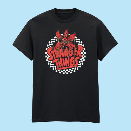A black short-sleeve crewneck t-shirt featuring a circular graphic on the chest with a red flower, the words 'STRANGER THINGS' in red, and a black-and-white checkered circle background.