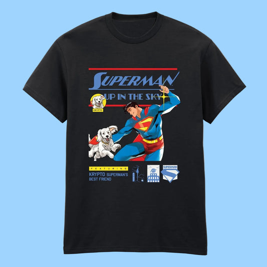 A black short-sleeve t-shirt featuring a colorful graphic print of Superman flying with a white dog, with retro-style text reading 'SUPERMAN UP IN THE SKY' and 'KRYPTO SUPERMAN'S BEST FRIEND'.