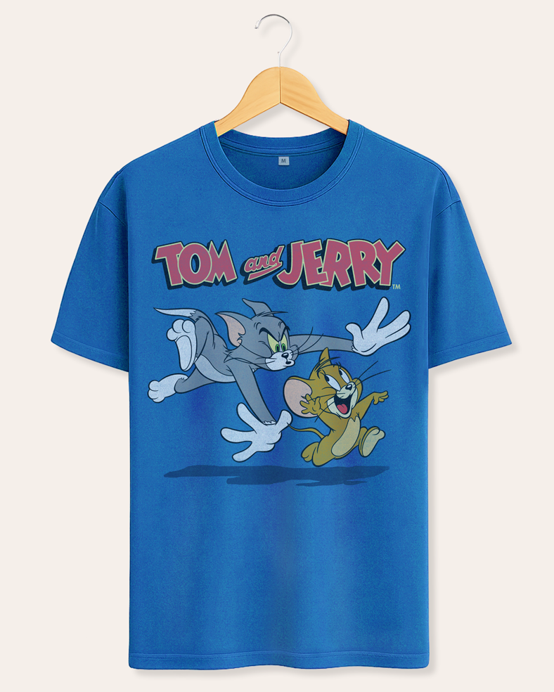 A blue short-sleeve crewneck t-shirt hanging on a wooden hanger against a light beige background. The shirt features a large graphic print of Tom and Jerry cartoon characters running underneath the 'TOM AND JERRY' logo.