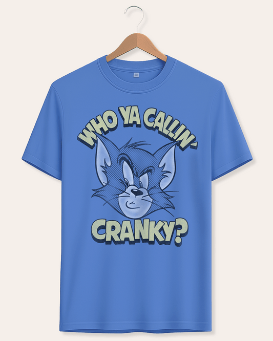 A blue short-sleeve graphic t-shirt hanging on a wooden hanger against a light beige background. The shirt features a cartoon illustration of Tom Cat's face with the text 'WHO YA CALLIN' above and 'CRANKY?' below in a bold, stylized font.