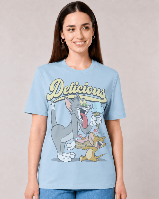 A woman wearing a light blue graphic t-shirt featuring Tom and Jerry cartoon characters with the word 'Delicious' in yellow script, set against a neutral beige background.