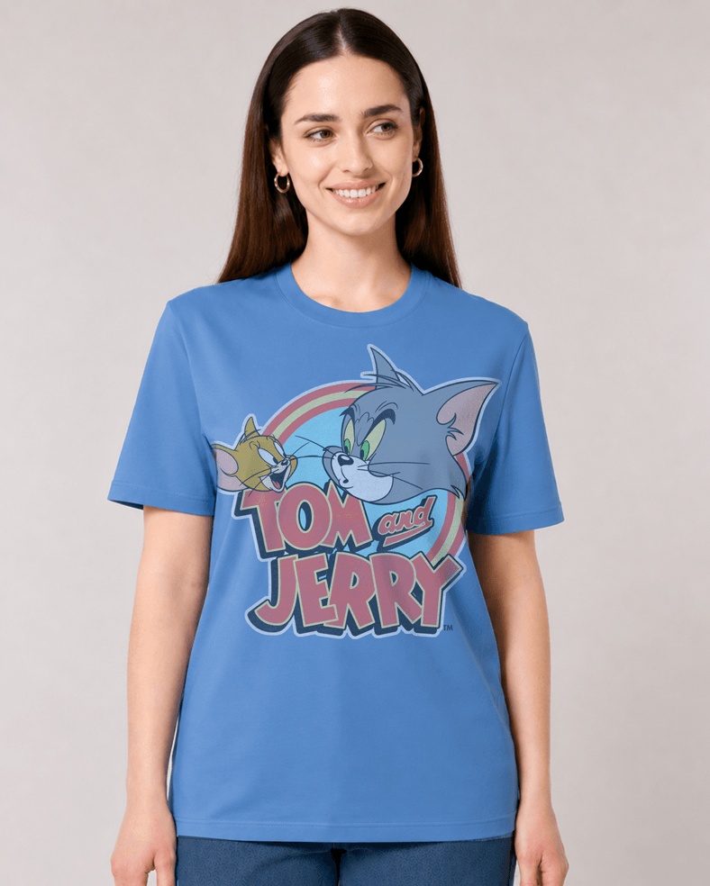 A woman wearing a blue short-sleeve graphic t-shirt featuring Tom and Jerry cartoon characters and the 'Tom and Jerry' logo on the front, set against a plain light gray studio background.
