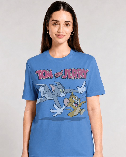A woman wearing a blue graphic t-shirt featuring the 'Tom and Jerry' cartoon characters, set against a plain light gray studio background.