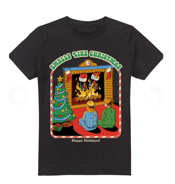 A black cotton crewneck t-shirt featuring a colorful graphic print of a cozy Christmas scene with two children sitting by a fireplace, a decorated tree, and the text 'SMELLS LIKE CHRISTMAS' and 'Happy Holidays!'.