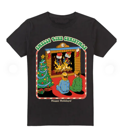 A black cotton crewneck t-shirt featuring a colorful graphic print of a cozy Christmas scene with two children sitting by a fireplace, a decorated tree, and the text 'SMELLS LIKE CHRISTMAS' and 'Happy Holidays!'.