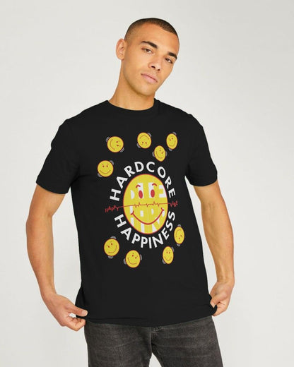 A man wearing a black short-sleeve t-shirt with a graphic print featuring a yellow smiley face, smaller yellow smiley faces around it, and the words 'HARD CORE HAPPINESS' in white. He is standing against a light gray studio background.