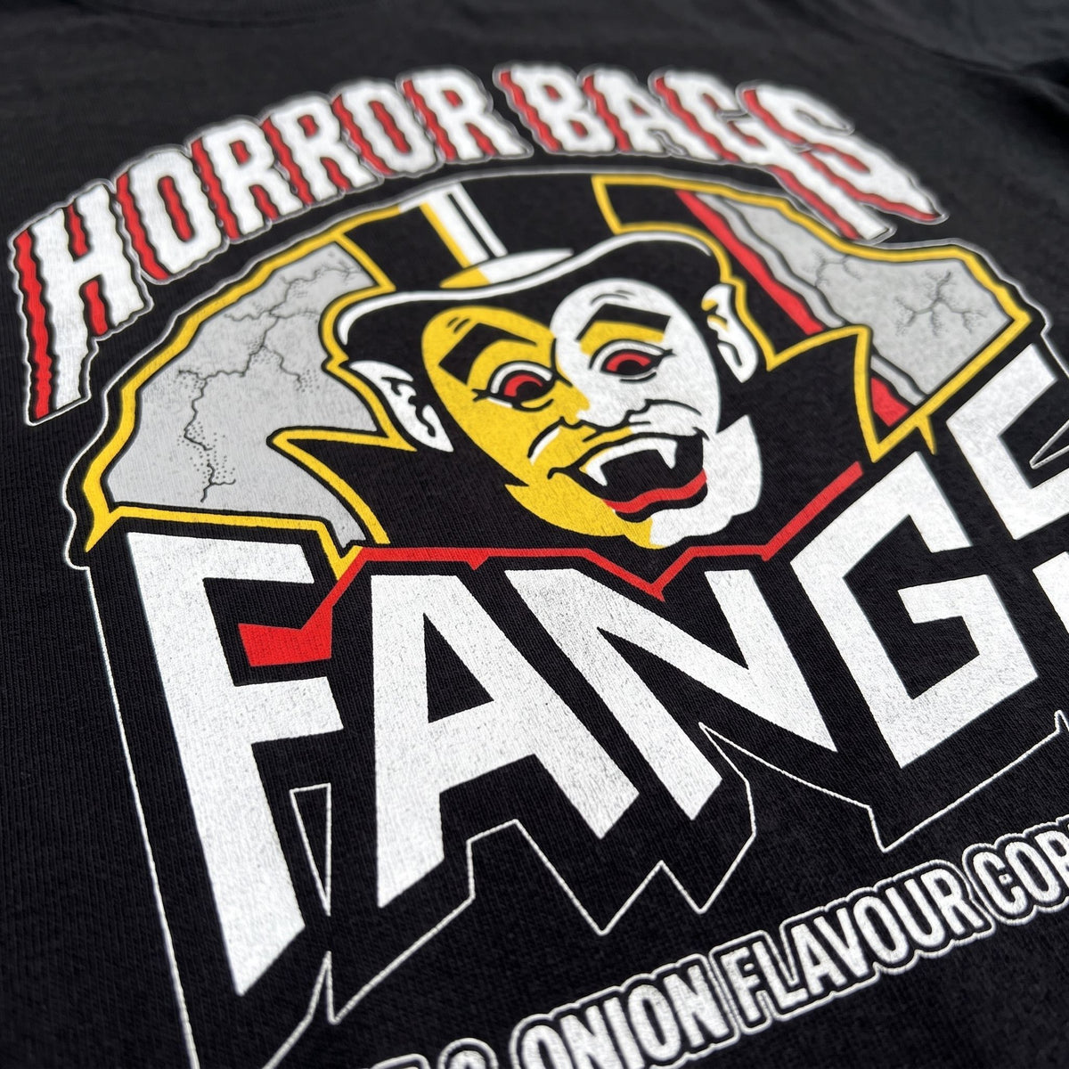 Close-up of a black graphic t-shirt featuring a stylized vampire face and the words 'HORROR BAGS FANGS' in distressed white, red, and yellow print.